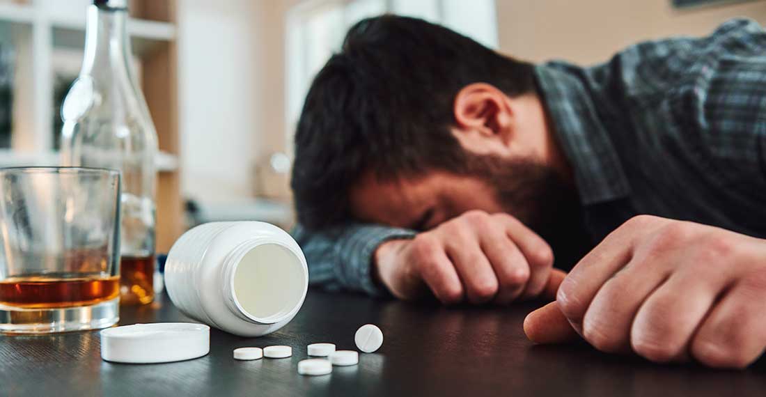 пьяный мужчина спит за столом рядом с таблетками и стаканом с алкоголем