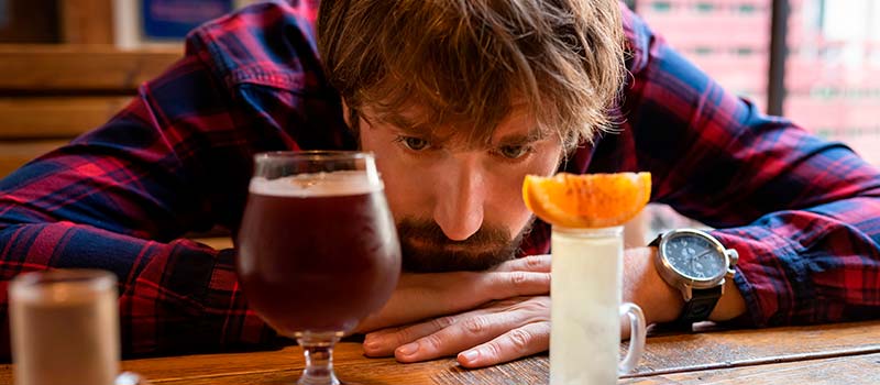 грустный мужчина сидит за столом с алкоголем